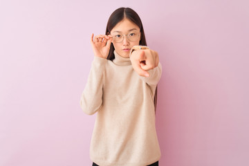 Young chinese woman wearing turtleneck sweater and glasses over isolated pink background pointing with finger to the camera and to you, hand sign, positive and confident gesture from the front