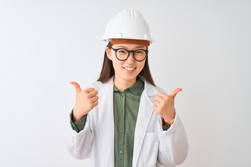 Young chinese engineer woman wearing coat helmet glasses over isolated white background success sign doing positive gesture with hand, thumbs up smiling and happy. Cheerful expression