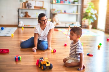 Fototapeta premium Beautiful teacher and toddler boy playing with tractor and cars at kindergarten