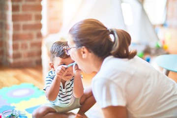 Beautiful toddler boy sitting on puzzle playing with plastic plates, fruits and vegetables at kindergarten