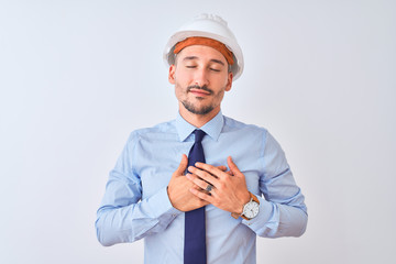 Young business man wearing contractor safety helmet over isolated background smiling with hands on chest with closed eyes and grateful gesture on face. Health concept.