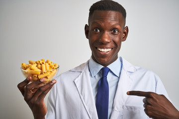 African american doctor man holding bowl with macaroni pasta over isolated white background with surprise face pointing finger to himself