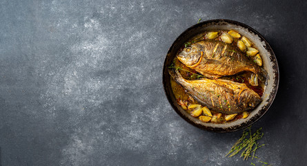 Obraz na płótnie Canvas Baked sea bream or dorada with onion and herbs in pan on dark background