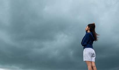Young woman wearing loose long-sleeved sweater over stormy cloudscape, Beauty and youth