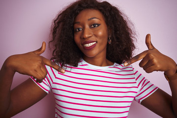 Young african american woman wearing striped t-shirt standing over isolated pink background looking...