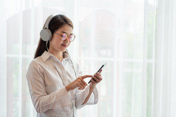 Young Asian woman enjoy listening to music with headphones while holding mobile phone, happy and relaxing time