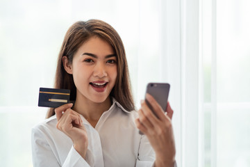 Young Asian woman holding credit card and thinking of online shopping in internet