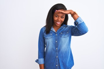 Beautiful young african american woman wearing denim jacket over isolated background very happy and smiling looking far away with hand over head. Searching concept.