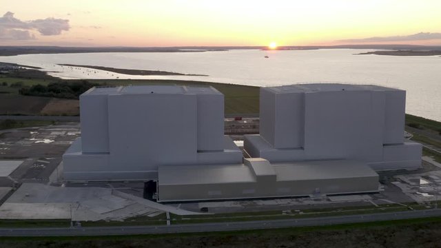 Nuclear power station with gorgeous golden sunset by a river, drone high angle.