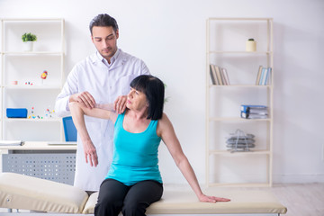 Young male doctor examining old female patient