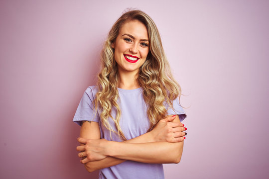 Young beautiful woman wearing purple t-shirt standing over pink isolated background happy face smiling with crossed arms looking at the camera. Positive person.