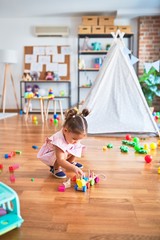 Young beautiful toddler sitting on the floor playing with wooden train toy at kindergaten
