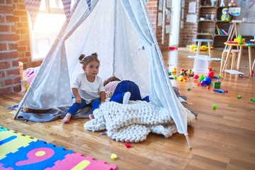 Adorable toddlers lying down over blanket inside tipi smiling at kindergarten