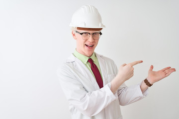 Albino scientist man wearing glasses and helmet standing over isolated white background amazed and smiling to the camera while presenting with hand and pointing with finger.