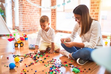 Fototapeta premium Beautiful teacher and toddler playing with building blocks around lots of toys at kindergarten