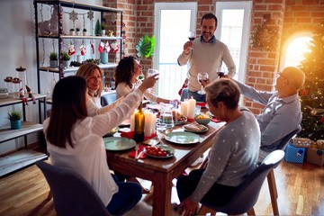 Family and friends dining at home celebrating christmas eve with traditional food and decoration, making a toast for new year best wishes