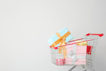 Shopping cart with gifts near light wall