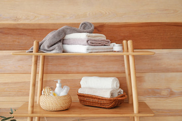 Shelf unit with bath supplies and towels near wooden wall