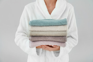 Woman holding stack of towels on light background - Powered by Adobe