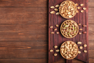 Bowls with tasty pistachio nuts on wooden background