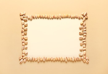 Frame made of tasty pistachio nuts on color background