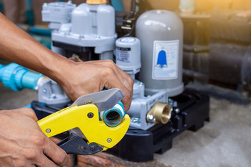 Technician worker man hand using pvc pipe cutter or scissors for cutting the piece of blue water pvc pipe with water pump blur background at workplace. Maintenance concept.