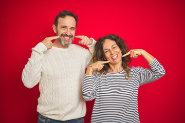 Beautiful middle age couple wearing winter sweater over isolated red background smiling cheerful showing and pointing with fingers teeth and mouth. Dental health concept.