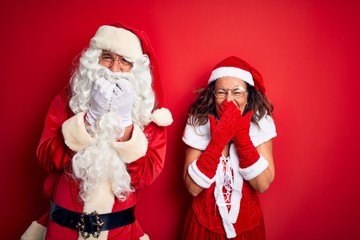 Middle age couple wearing Santa costume and glasses over isolated red background laughing and...