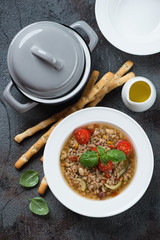 Top view of italian spelt and minestrone soup over grey cracked stone background, vertical shot