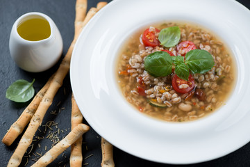 Closeup of spelt and minestrone soup served in a white plate, selective focus, studio shot