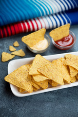 Close-up of a white plate with nachos chips and dips, blue stone surface with mexican poncho in the background