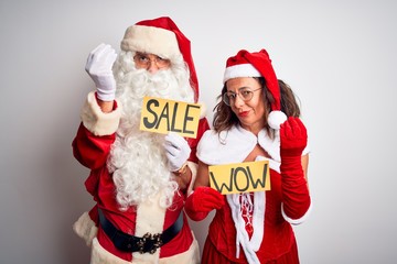 Couple wearing Santa costume holding wow and sale banner over isolated white background Doing Italian gesture with hand and fingers confident expression