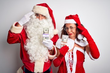 Senior couple wearing Santa Claus costume holding dollars over isolated white background Shooting and killing oneself pointing hand and fingers to head like gun, suicide gesture.