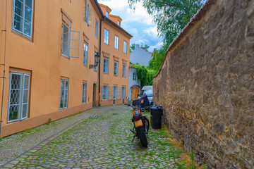 Narrow, empty, cozy street of an old European city with houses and a motorcycle parked near a wall.