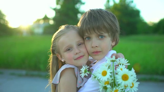 Portrait of little cute boy and pretty girl hugging with bouquet of chamomile on summer. Happy family outdoors. Brother and sister children hug, having fun at sunset. childhood first love, friendship