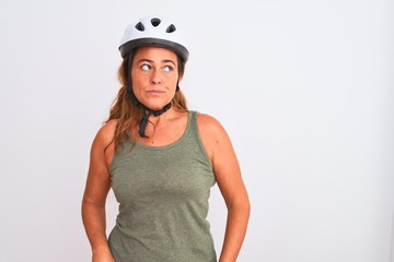 Middle age mature cyclist woman wearing safety helmet over isolated background smiling looking to the side and staring away thinking.
