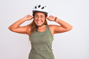 Middle age mature cyclist woman wearing safety helmet over isolated background Smiling pulling ears with fingers, funny gesture. Audition problem