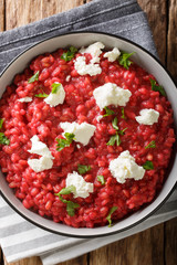 Orzotto with beets, parmesan, goat cheese and herbs close-up on a plate. Vertical top view