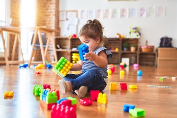 Beautiful toddler sitting on the floor playing with building blocks toys at kindergarten