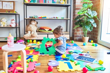 Beautiful toddler sitting on the floor playing with building blocks toy at kindergarten