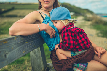 Young mother breastfeeding her toddler on bench by the sea