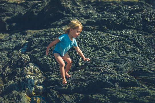 Little toddler playing on the rocks in summer