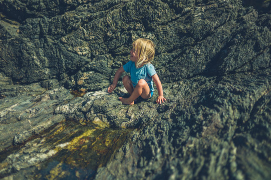 Little toddler playing on the rocks in summer
