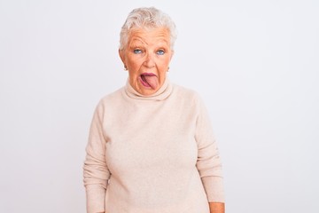 Senior grey-haired woman wearing turtleneck sweater standing over isolated white background sticking tongue out happy with funny expression. Emotion concept.