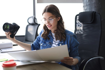 Young architect holding digital camera and looking on blueprint while working in the creative office.
