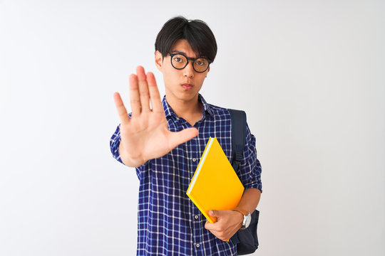 Chinese student man wearing backpack holding notebook over isolated white background with open hand doing stop sign with serious and confident expression, defense gesture