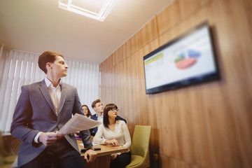 Meeting of office workers at the table, looking at the presentation with diagrams on the TV