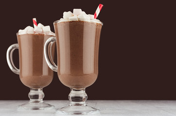 Luxury sweet chocolate dessert in wineglass with marshmallows and red striped straw on dark brown background, copy space.