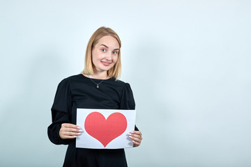 Portrait of cheerful girl in casual clothes holding red heart with copy space isolated on blue turquoise background. People sincere emotions, lifestyle concept.