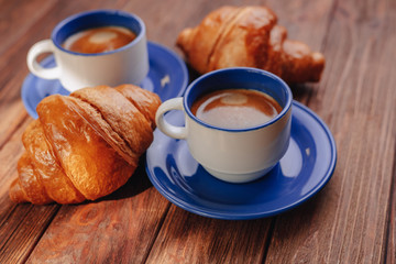 two cups of coffee and croissants on a wooden background, good light, morning atmosphere